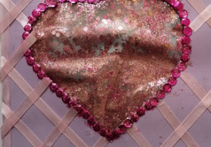 Zdjęcie przedstawia brokatowe serce w różowej otoczce wykonanej z cekinów na fioletowym tle z różowymi paskami ułożonymi w kształcie szachow