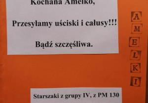 Na pomarańczowej kartce widnieje napis: „Kochana Amelko przesyłamy uściski i buziaki. Bądź szczęśliwa. Straszaki z grupy 4 z PM nr 130 w Łodzi”.