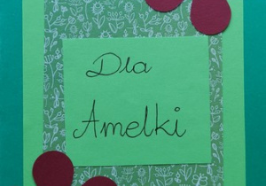Niebieska kartka, na której znajdują się dwa filetowe kwiaty oraz napis: „Dla Amelki”.