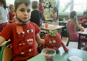 Zdjęcie ucznia klasy 1a z pysznymi, świeżymi truskawkami i truskawką-pluszakiem, którą przyniósł do szkoły.