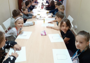 Zdjęcie dzieci z klasy 2a siedzących przy stolikach w czasie warsztatów plastycznych.