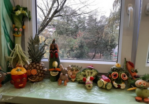 Postacie wykonane z owoców i warzyw ustawione na oknie.