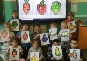 Grupa dzieci prezentuje swoje prace na tle kolorowych warzyw.