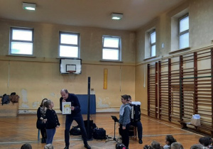 Dwie osoby i dziecko stojące na środku sali gimnastycznej.