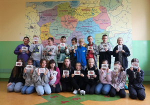 Uczniowie ustawieni w grupie. Trzymają kartki pocztowe. W tle mapa Polski.