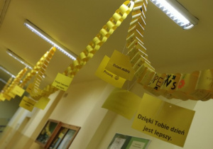Zdjęcie 6 Żółty łańcuch z przywieszonymi kartkami: dzięki tobie dzień jest lepszy, dzień dobry, proszę. W tle szkolny korytarz.
