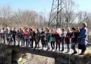Uczniowie stoją na mostku nad rzeczką.