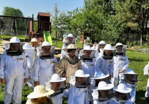 Uczniowie klas drugich w kombinezonach pszczelarskich.