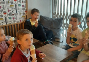 Czterech chłopców i jedna dziewczynka siedzą przy stoliku i jedzą lody.