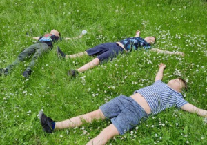 Uczniowie leżą na trawie, odpoczywają.