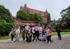 Uczniowie pozują do zdjęcia. W tle Zamek Malbork.