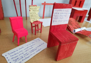 Czerwone krzesła wykonane przez uczniów. W tle instrukcja obsługi.