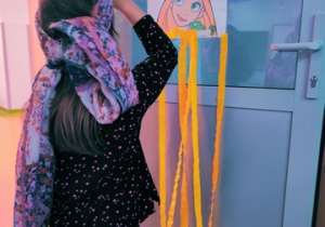 Dziewczynka przykleja imitację włosów z bibuły.